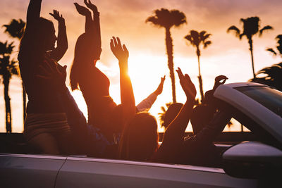 Group of friends enjoying road trip in convertible car during sunset