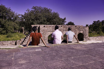 Rear view of men sitting in park against sky