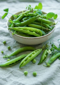 Bowl with young fresh juicy pods of green peas on a textile background. healthy organic food.