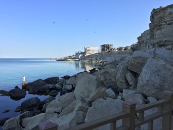 Rocks by sea against clear blue sky