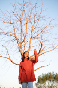 Portrait of woman standing by bare tree against sky
