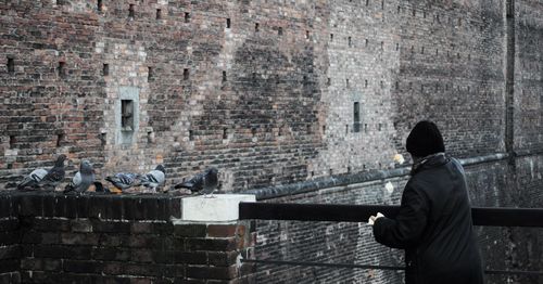 Rear view of woman standing by pigeons at castle