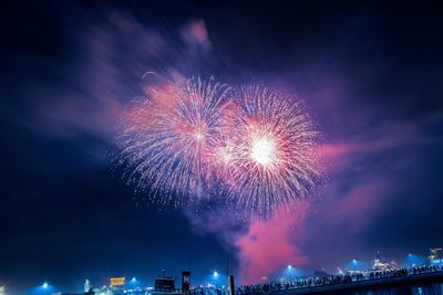 Illuminated firework display in city against sky at night