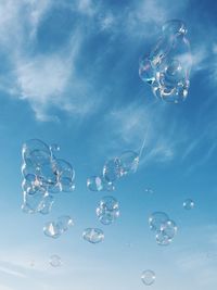 Low angle view of bubbles flying against blue sky