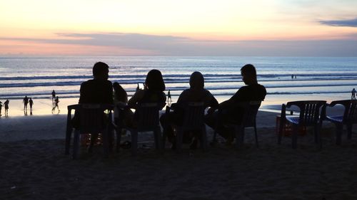 Silhouette people sitting on beach against sky during sunset