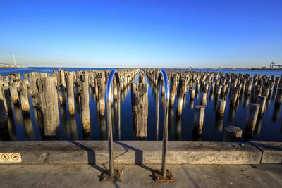 Panoramic view of wooden posts in princes pier in sea against clear blue sky