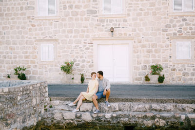 Full length of couple sitting against building