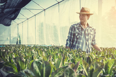 Young man looking away while standing against plants