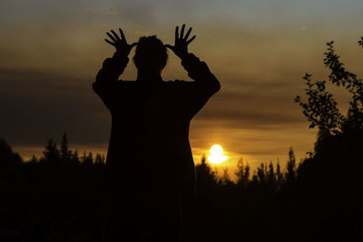 Silhouette woman with arms raised standing against sky during sunset