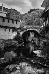 Arch bridge over river amidst buildings against sky