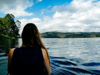 Rear view of woman sitting on boat in lake against cloudy sky