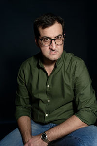 Portrait of man sitting against black background
