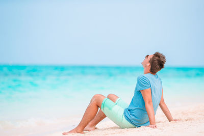 Man sitting on shore at beach against sky