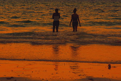 Rear view of women standing at beach during sunset