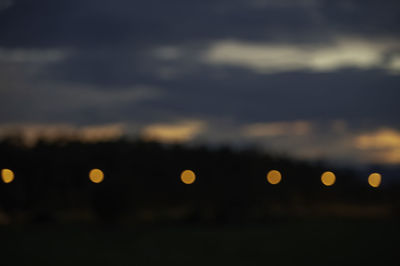 Defocused image of illuminated lights against sky at night