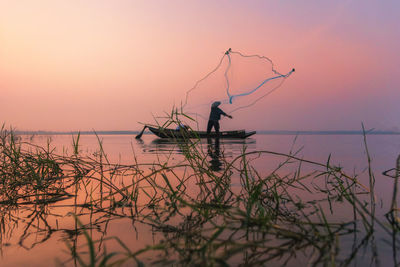 Silhouette man fishing by sea against sky during sunset