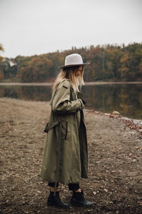 Side view of woman wearing hat standing by lake against sky