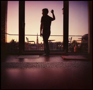 Silhouette man standing by city against sky during sunset