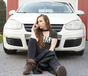 Young woman sitting against car