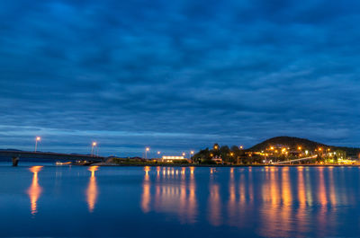 Illuminated buildings by sea against sky at night