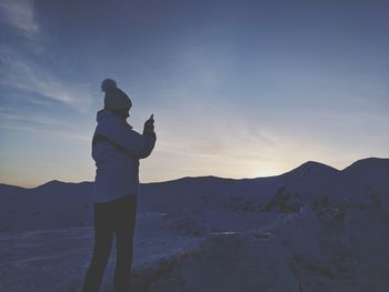 Woman standing on snow covered land against sky during sunset