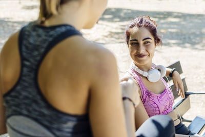 Happy diverse sportswomen resting on a bench in city park