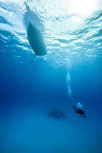 Scuba diver swimming below boat undersea