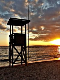 Silhouette lifeguard hut at beach against cloudy sky during sunset