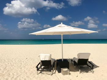Deck chairs on beach against sky on sunny day