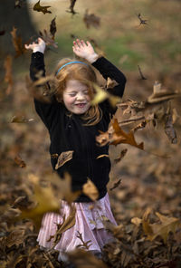 Autumn leaves falling on girl with arms raised standing at park