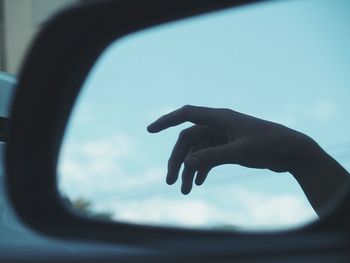 Reflection of human hand against sky seen in side-view mirror of car