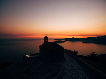 Lighthouse by sea against sky during sunset