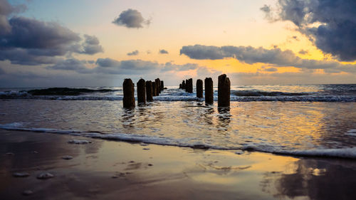 Wooden posts on beach against sky during sunset