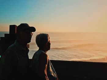 People looking at sea against sky during sunset