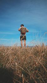 Rear view of young man with backpack standing at beach against sky