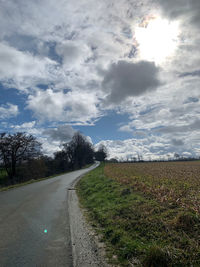 Empty road amidst field against sky