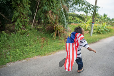 Rear view full length of boy with malaysian flag walking on road 