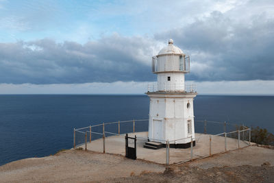White lighthouse on the mountain against the background of the sea and the stormy sky.  meganom
