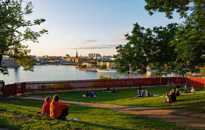 People sitting on riverbank against sky