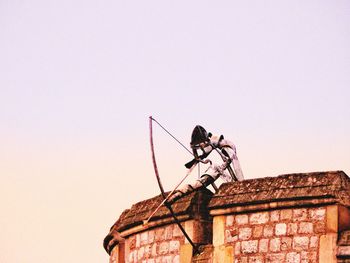 Low angle view of man working on building against clear sky