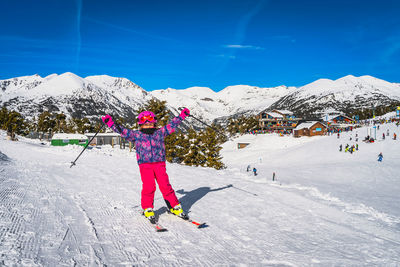 Young girl on a ski lifting her hands up in a cheer, ski resort and mountains in background, andorra