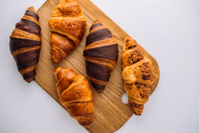 Flat lay of bunch of appetizing brown and chocolate croissants on a wooden board on white table