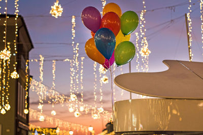 Low angle view of colorful balloons with illuminated lighting equipment hanging against sky at dusk