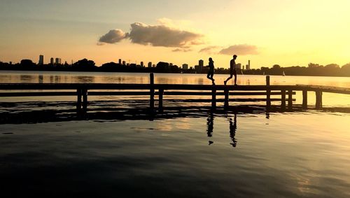 Silhouette people on wooden post by sea against sky during sunset