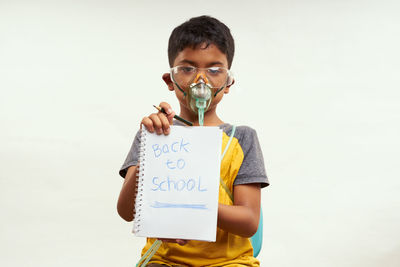 Portrait of boy holding camera while standing against clear sky