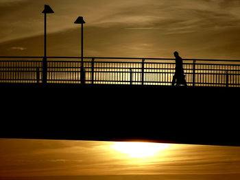 Silhouette man standing on bridge against sky during sunset