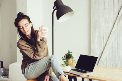 Portrait of young woman using phone while sitting on table