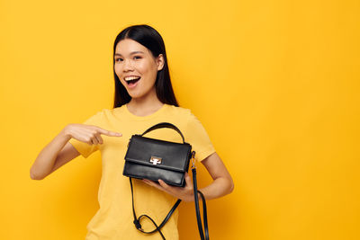 Young woman holding suitcase against yellow background