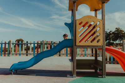 Baby girl playing on slide at playground against cloudy sky