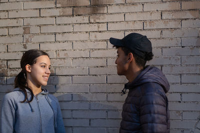 Young couple talking and smiling standing against a brick wall. love signals between teenagers